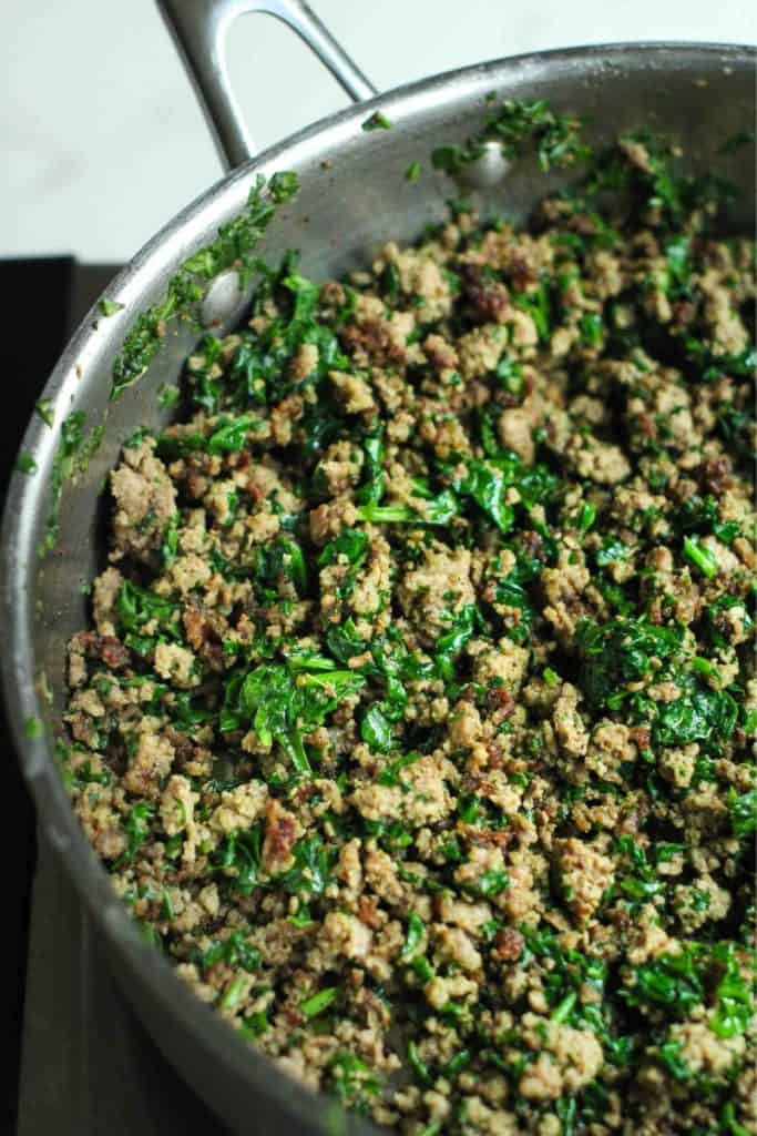 Ground beef and spinach sauteed in a stainless steel pan.