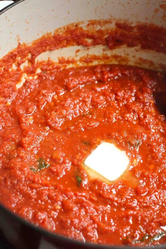 Marinara sauce in a dutch oven with a pad of butter in the middle before being stirred in.