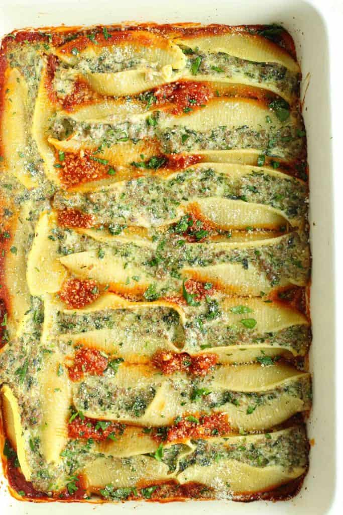 Beef stuffed shells lined over marinara sauce topped with grated parm and chopped parsley in a white baking dish.