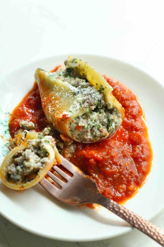 A beef stuffed shell with a fork full cut out over a bed of marinara sauce on a white plate.