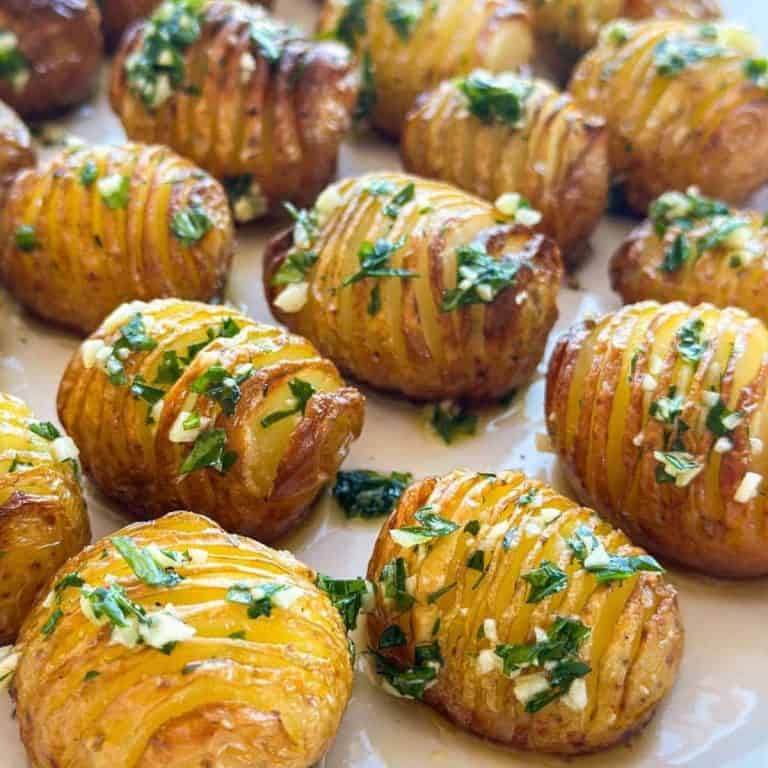 Christmas dinner side dishes hassleback potatoes topped with garlic and parsley lined on a white baking dish.