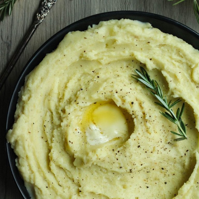 Christmas dinner side dishes rosemary garlic mashed potatoes with a slab of butter in the center and a spring of rosemary.