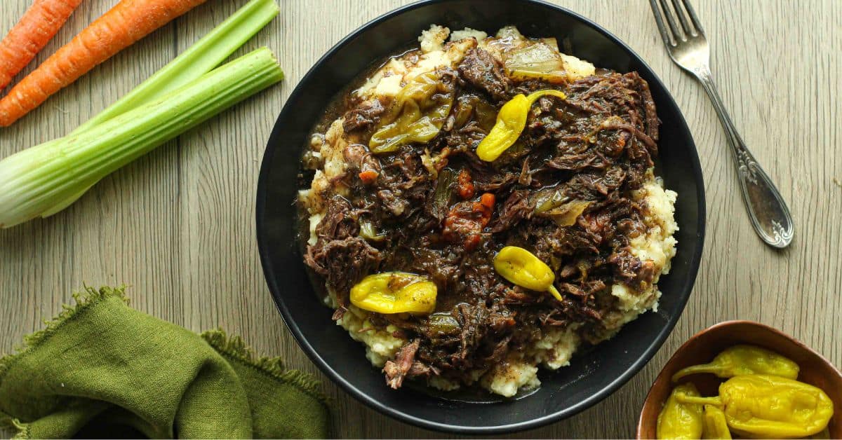 Mississippi pot roast over mashed potatoes topped with peperoncinis in a black bowl.