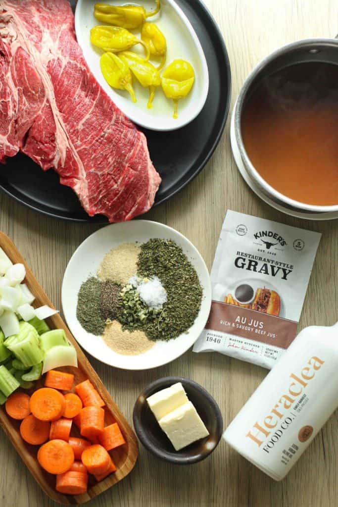 Instant pot mississippi pot roast ingredients set on a wooden board: butter, olive oil, seasonings, veggies, chuck roast, pepperocinis.
